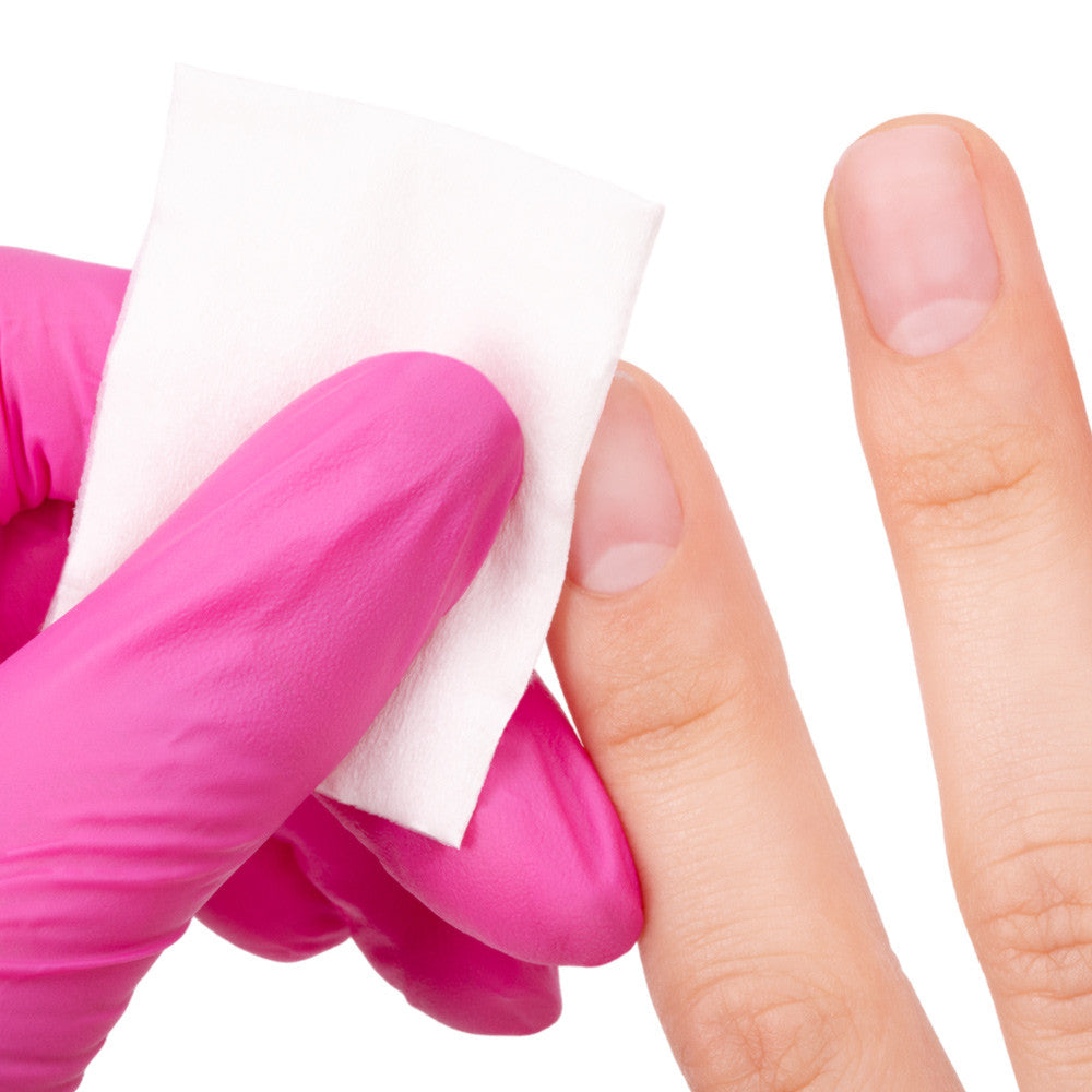 Hand wearing a pink glove holding a white cotton pad against a white background
