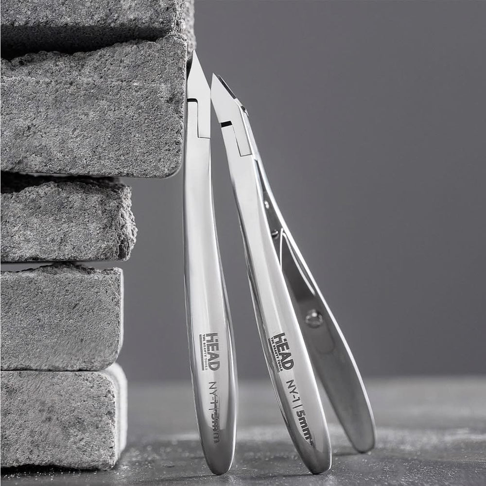 Metal nail clippers leaning against a stone wall on a gray surface.